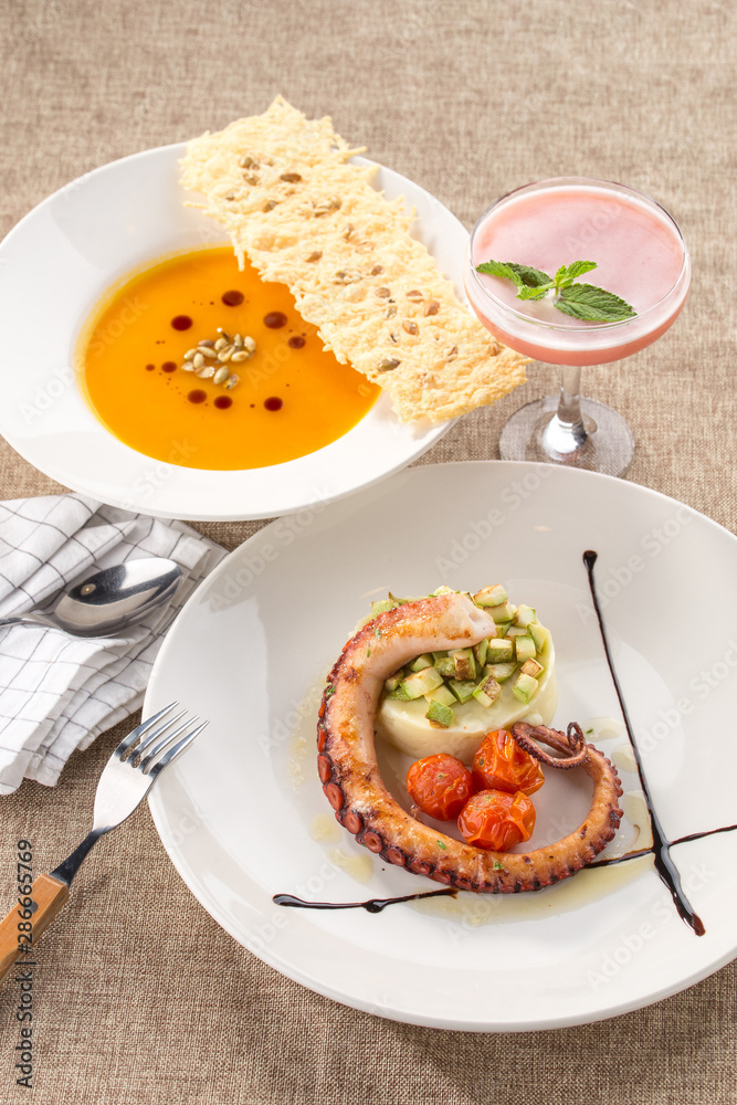 lunch set pumpkin cream soup and grilled octopus with potato and pink cocktail on the table