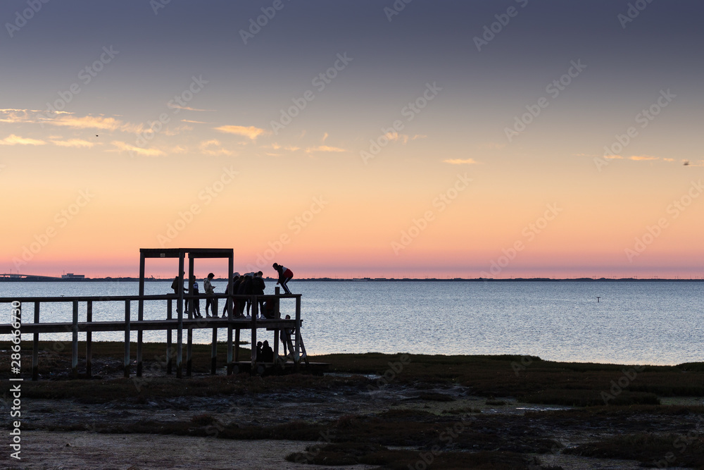 Boys watching the sunset from old wooden jetty
