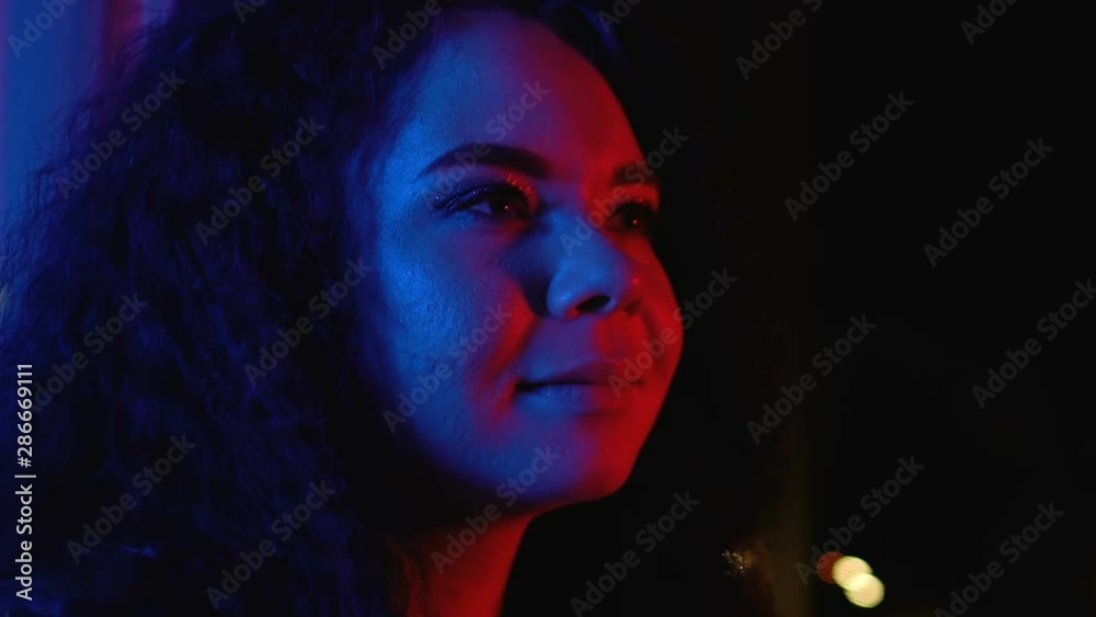 Young smiling woman watching night city lights enjoying home party, relaxing Young smiling woman watching night city lights enjoying home party, relaxing