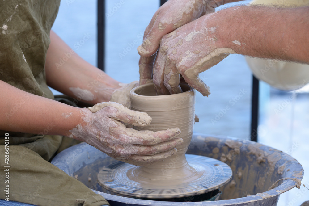 Teaching of wheel throwing. Potter’s hand correcting woman’s ones during shaping clay blank on a potter's wheel