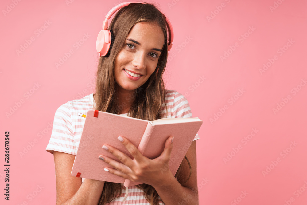Image of pretty beautiful girl writing down notes at diary book and listening to music with headphones Image of pretty beautiful girl writing down notes at diary book and listening to music with headphones
