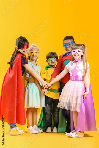 Cute little children dressed as superheroes on color background