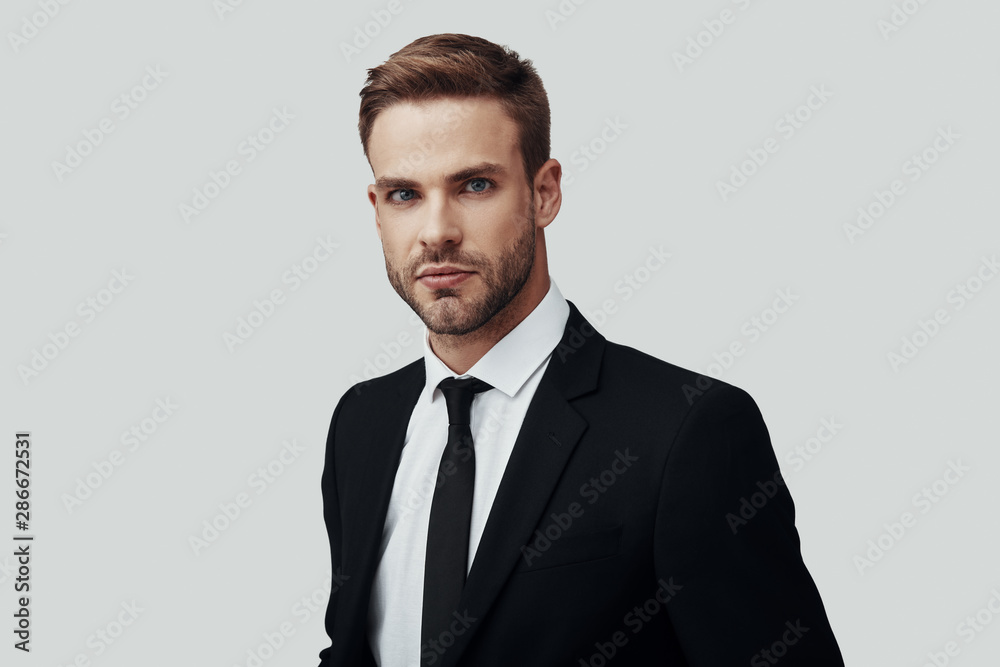 Handsome young man in formalwear looking at camera while standing against grey background Handsome young man in formalwear looking at camera while standing against grey background