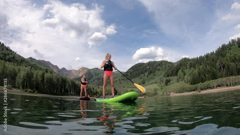 Teenage girls paddle boarding on Sliver Lake Flats in Utah on hot summer day.
