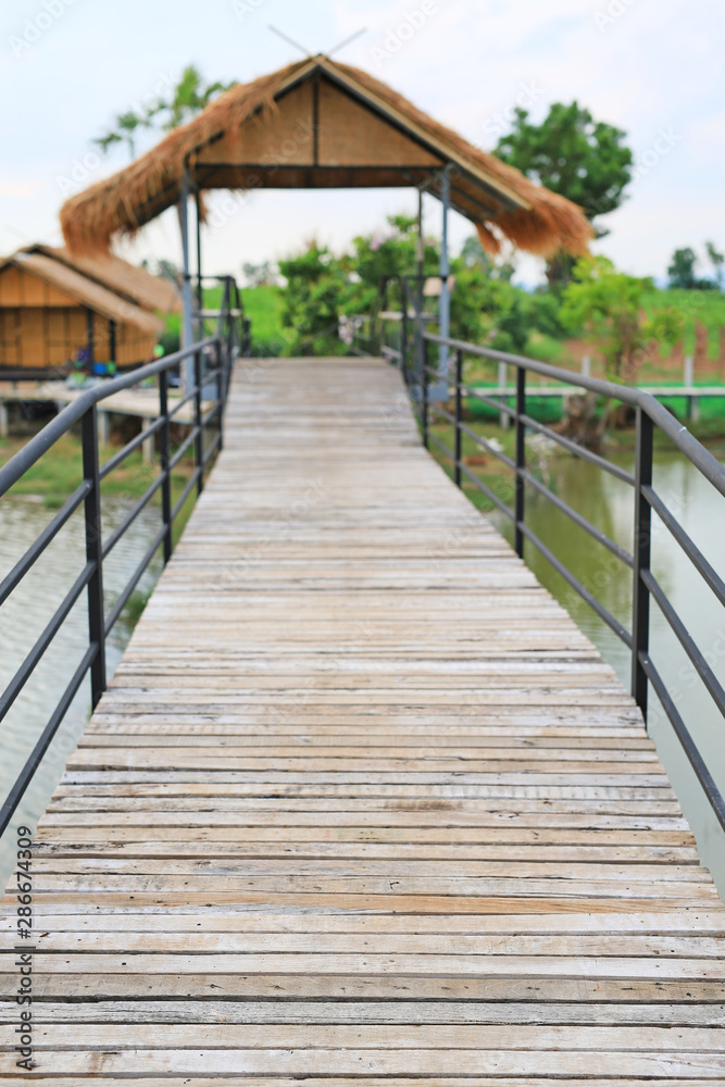 Wooden bridge crossing river to countryside pavilion in Thailand.