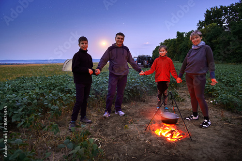 Family traveling and camping, twilight, cooking on the fire. Beautiful nature - field, forest, stars and moon.