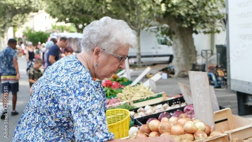 elderly senior woman buying fresh vegetables and fruits in farmer's market during summer day in provence france