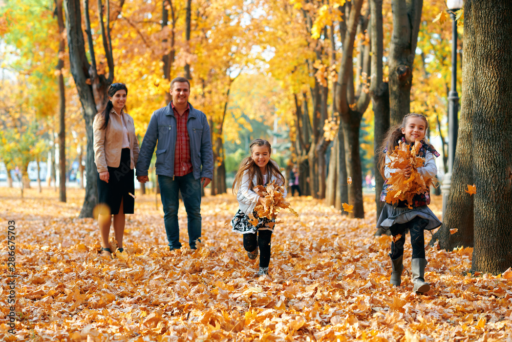 Happy family having holiday in autumn city park. Children and parents posing, smiling, playing and having fun. Bright yellow trees and leaves - obrazy, fototapety, plakaty 