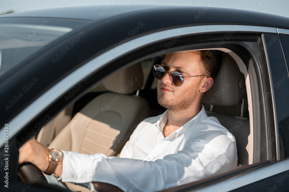 Happy driver in a white shirt and sun glasses drives his luxary car. Concept of success.