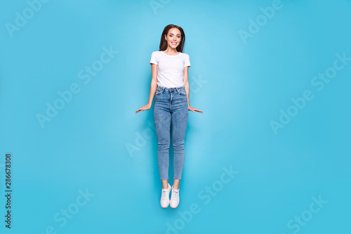 Full length photo of pretty youth jumping moving wearing white t-shirt jeans denim isolated over blue background