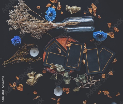 Tarot card spread on a nature display (flat lay) . Hand made tarot cards on a dark wooden table surrounded with dried herbs, blue flowers, white candles. Black cards with golden shiny rectangular rim