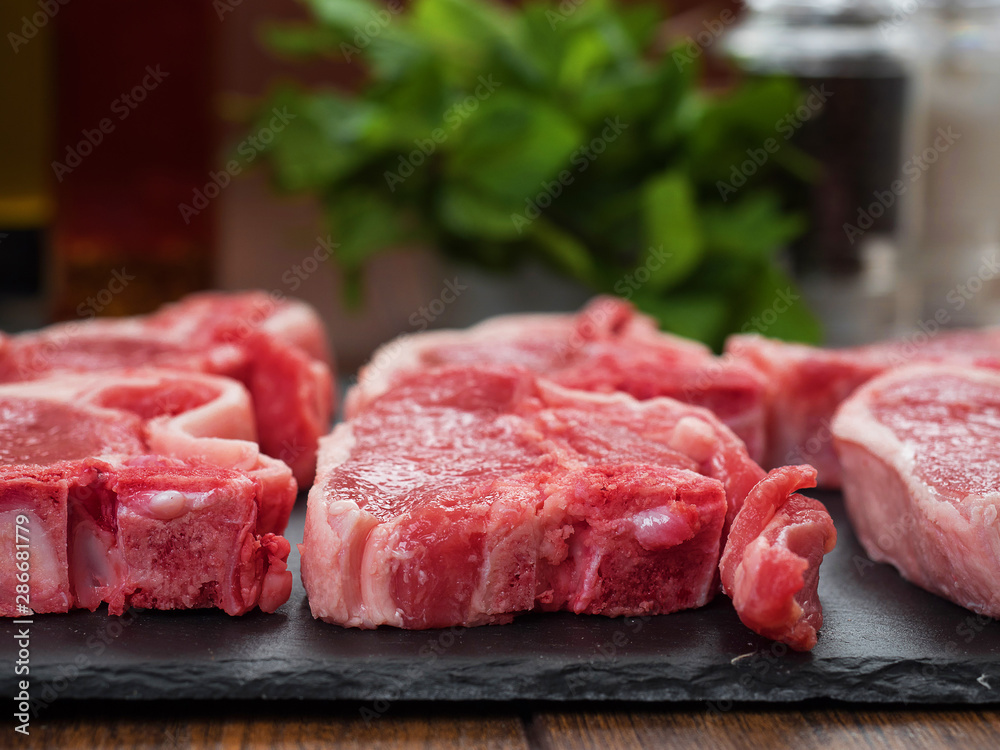 Fototapeta premium Fresh raw uncooked lamb chops in focus, Mint and pepper shaker out of focus.