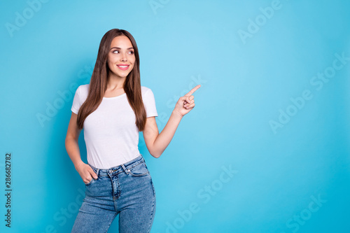 Portrait of pretty youth pointing at copy space looking at ads wearing white t-shirt denim jeans isolated over blue background