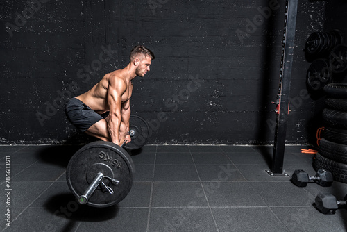 Young muscular sweaty man with big muscles doing barbell weight training workout in the gym dark image photo