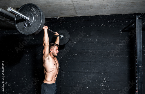 Young muscular sweaty man with big muscles doing barbell weight training workout in the gym dark image photo