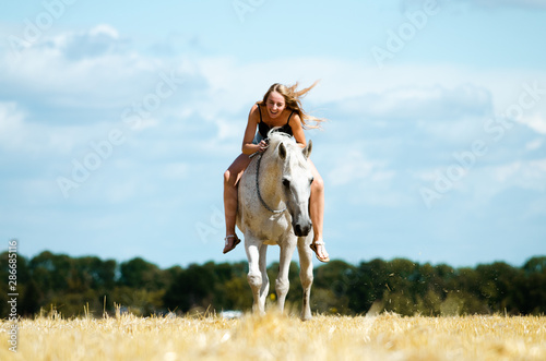 Reiterlin liegt lachend auf dem Hals ihres Pferdes, während es frontal auf die Kamera zugelaufen kommt