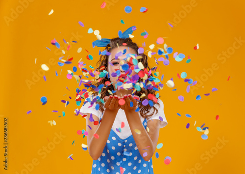cheerful funny young woman with festive confetti on yellow . photo