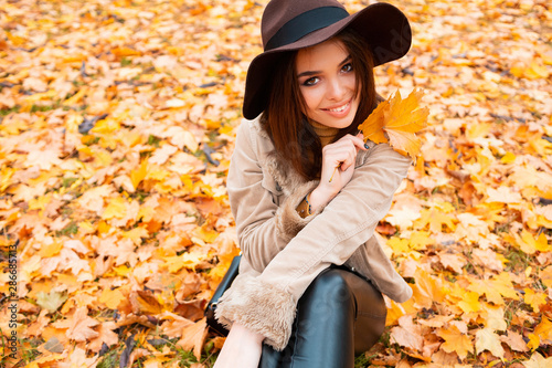 Carefree young woman in trendy vintage hat sitting in park and laughing. Curly cute girl in good mood posing in autumn day, enjoying good weather.season and people concept 