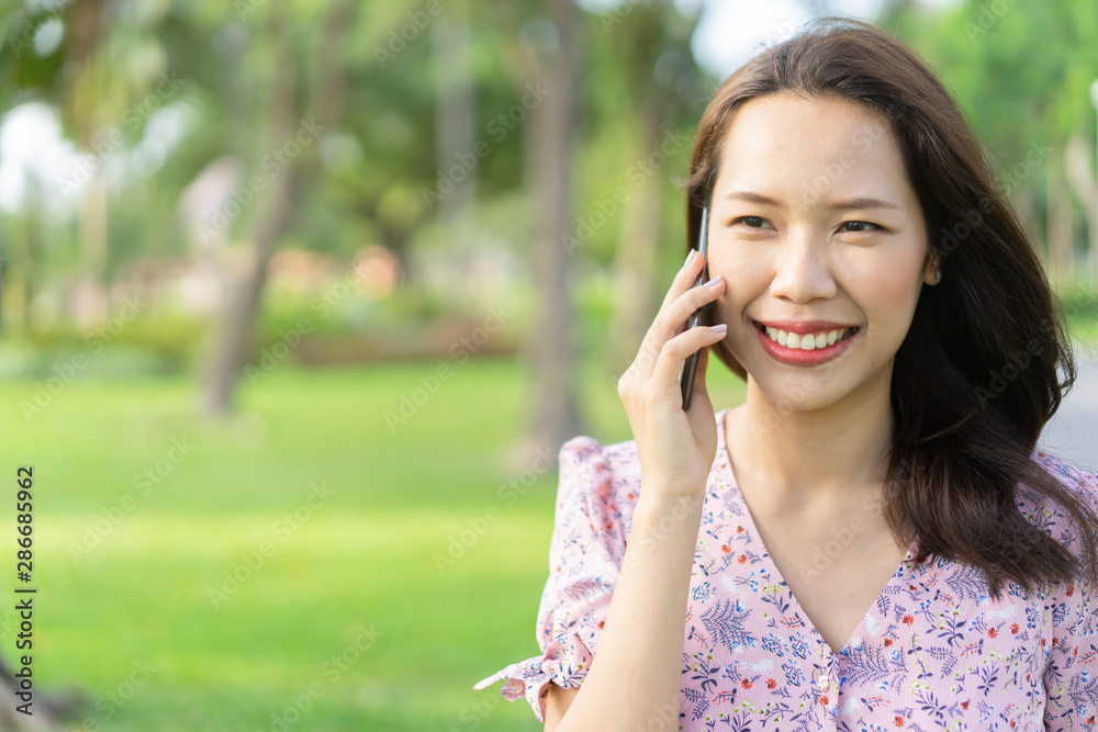 close up young beautiful asian woman smiling while talking via mobile phone at park outdoor in weekend for meeting friends in relaxing time , city lifestyle concept close up young beautiful asian woman smiling while talking via mobile phone at park outdoor in weekend for meeting friends in relaxing time , city lifestyle concept