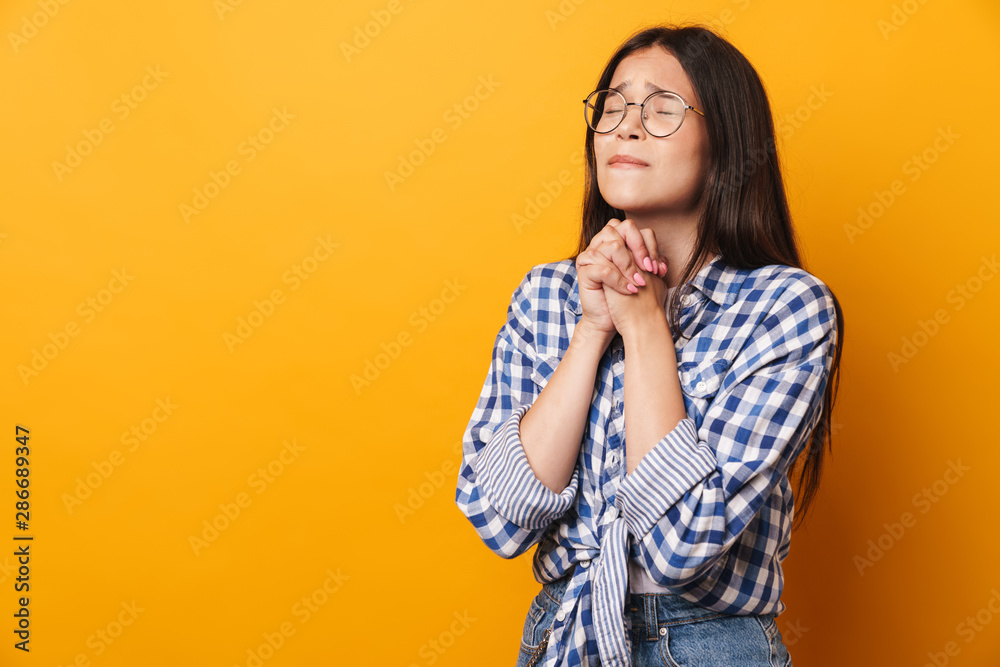 Nervous young cute teenage girl in glasses posing isolated over yellow wall background showing hopeful please gesture. Nervous young cute teenage girl in glasses posing isolated over yellow wall background showing hopeful please gesture.