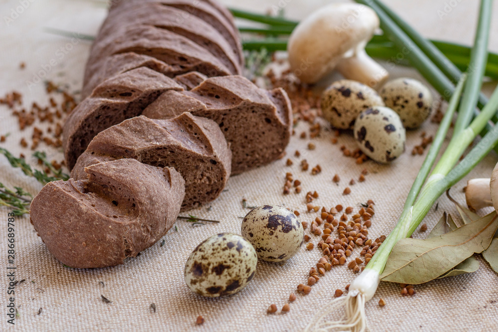 composition of dark sliced bread with scattered buckwheat, sprigs of rosemary, fresh mushrooms, quail eggs and green onions on baking canvas composition of dark sliced bread with scattered buckwheat, sprigs of rosemary, fresh mushrooms, quail eggs and green onions on baking canvas