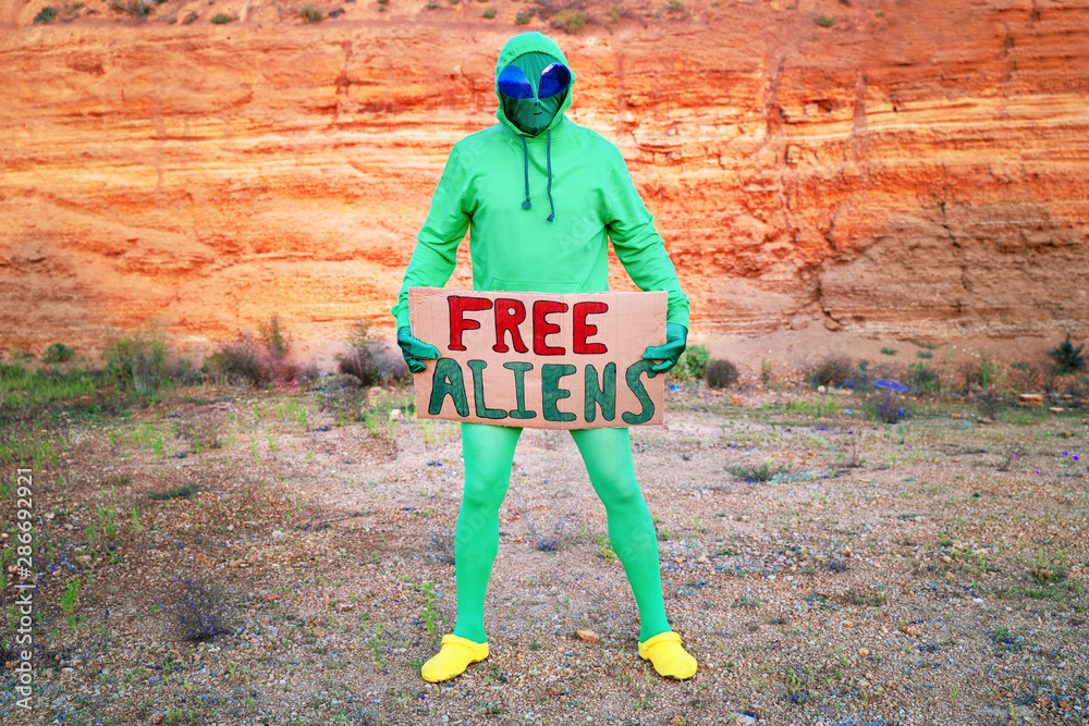 a man dressed in a green alien carnival costume suit at a lone rally with a  sign 