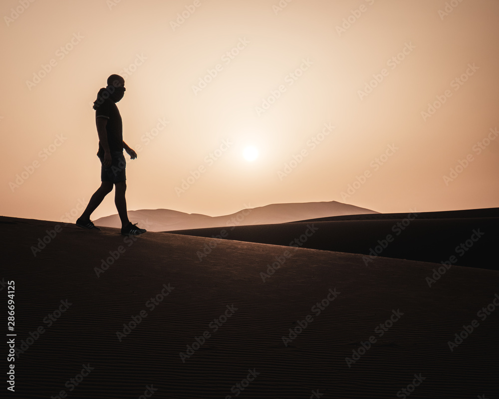 a man walking in the desert at sunrise in the Sahara Desert, Morocco