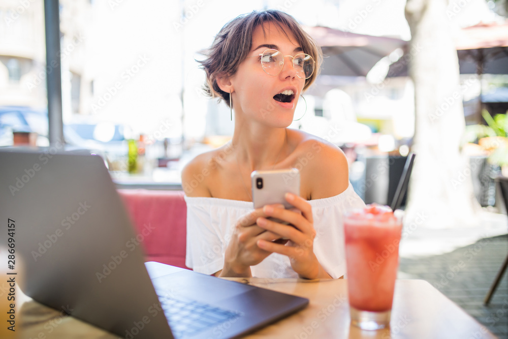 Surprised young woman with laptop and mobile phone in summer cafe Surprised young woman with laptop and mobile phone in summer cafe