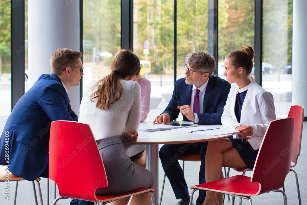 Colleagues discussing while sitting at table during meeting in office lobby