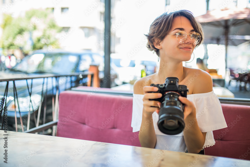 Young smiling woman look at pictures with a camera on the background of outdoor cafe Young smiling woman look at pictures with a camera on the background of outdoor cafe