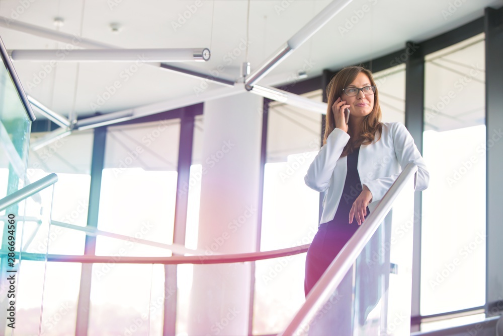 Low angle view of businesswoman talking on smartphone while standing at office Low angle view of businesswoman talking on smartphone while standing at office