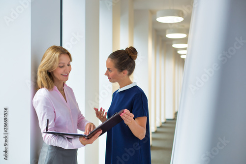 Businesswomen discussing over document while standing in corridor at office