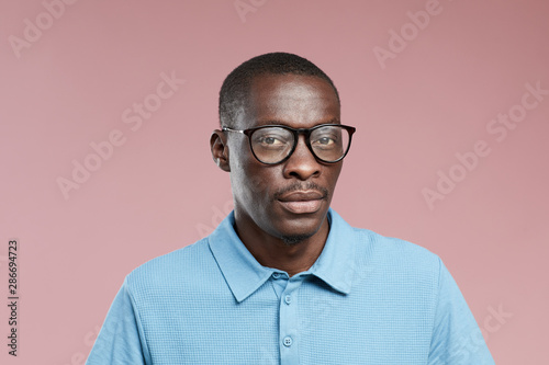 Portrait of African young man wearing eyeglasses and blue shirt looking at camera over pink background