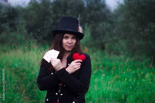 A woman in a tall hat with a red knitted heart and cards in her hands.