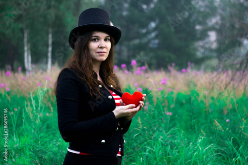 A woman in a tall hat with a red knitted heart in her hands. 