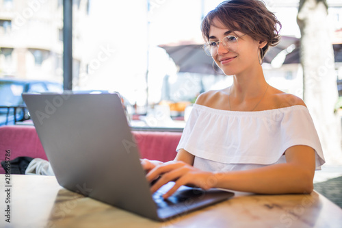 Smiling woman in cafe using laptop outdoors