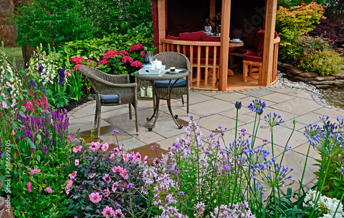 Fototapeta Naklejka Na Ścianę i Meble -  The patio area with seating in an aquatic garden with colourful flower border with dahlia, agapanthus, salvia, phlox, foxgloves and hydrangeas in front of a Summer House