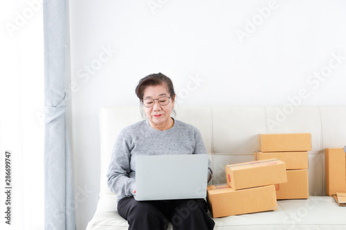 Asian senior woman retirement using laptop computer and packing box selling online market concept
