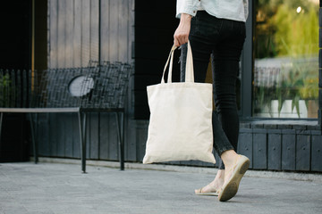 Woman holding white textile eco bag against urban city background. . Ecology or environment protection concept. White eco bag for mock up.