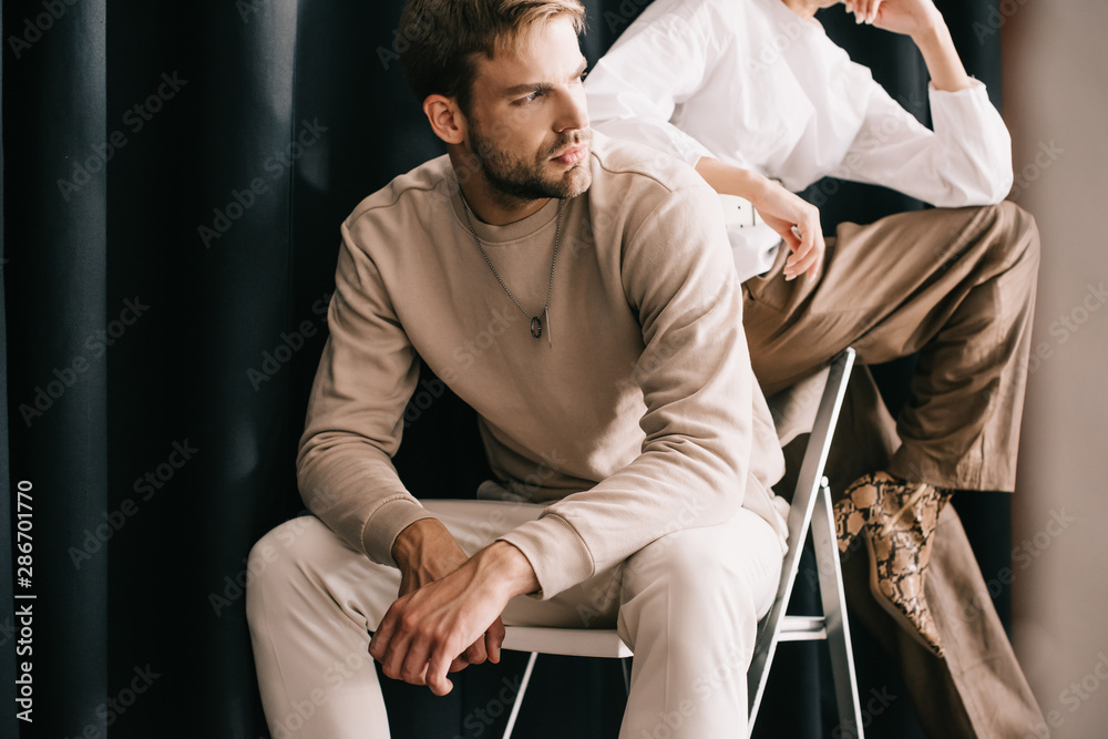 cropped view of woman in white blouse and bearded man sitting on chair near curtain