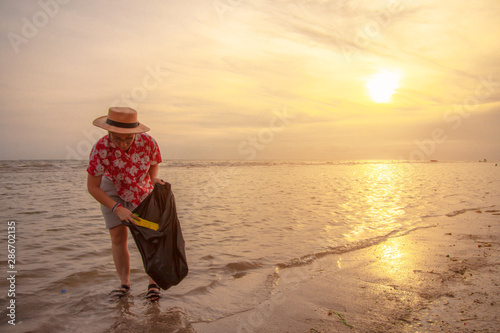 Asian women tourists picking up plastic garbage cleaning on the beach During the sunset . Tourists volunteers are helping to collect garbage picking up trash . Cleaning environmental pollution