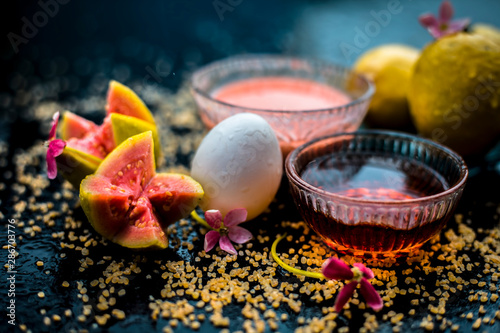 Guava face mask for dry skin on a wooden surface with vivid colors i.e., guava pulp, egg yolk, oatmeal, and some raw organic honey well mixed in a glass bowl along with raw ones. photo