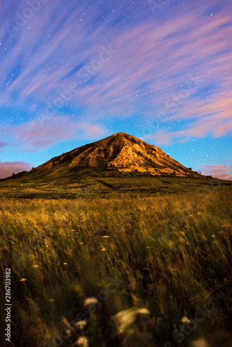 Mount Toratau against a starry sky and field with flowers in the foreground. Night photograph of stars and mountains. Clouds at night