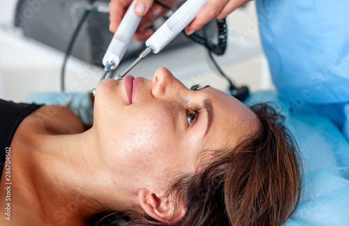 cosmetologist with a patient during facial procedures in a modern cosmetological and aesthetic clinic. A patient receives an electric facial massage. Skin rejuvenation and wrinkle smoothing.