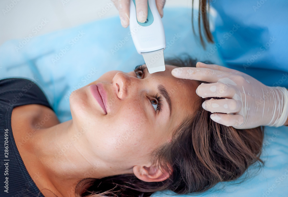 Naklejka premium cosmetologist with a patient during facial procedures in a modern cosmetological and aesthetic clinic. A patient receives an electric facial massage. Skin rejuvenation and wrinkle smoothing.