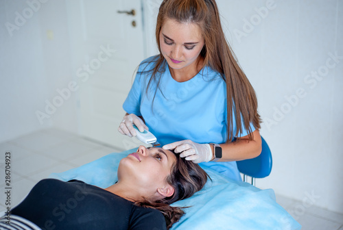 cosmetologist with a patient during facial procedures in a modern cosmetological and aesthetic clinic. A patient receives an electric facial massage. Skin rejuvenation and wrinkle smoothing.