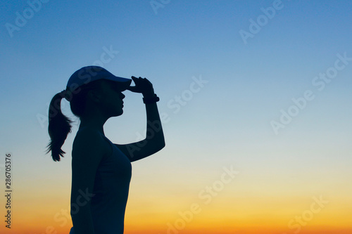 Silhouette of young girl over sunset sky background. People, travel, nature concept.