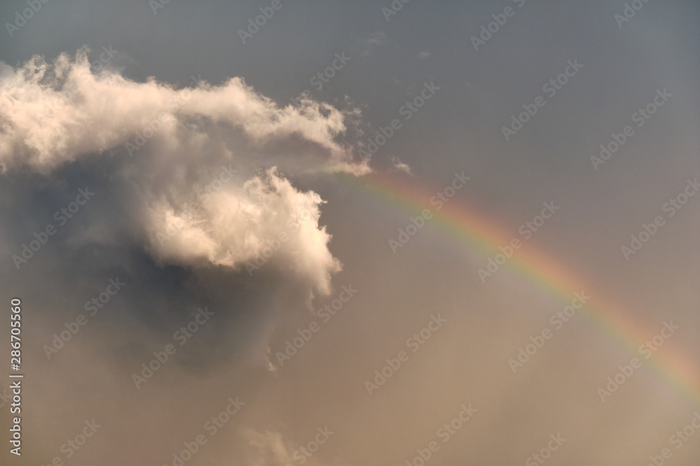 Beautiful scenery in the sky after a rainfall with a gray cloud in the sunshine and a rainbow on a gray sky