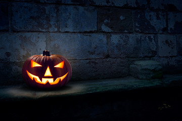 A single scary evil looking halloween Jack O Lantern on the left side of a dark blue stone plinth background of a haunted castle at night.