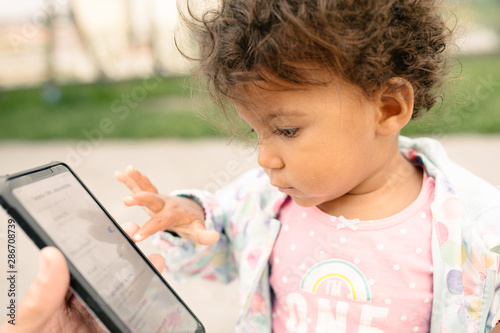 Fotografie Girl playing with a mobile phone touching the screen with her little finger